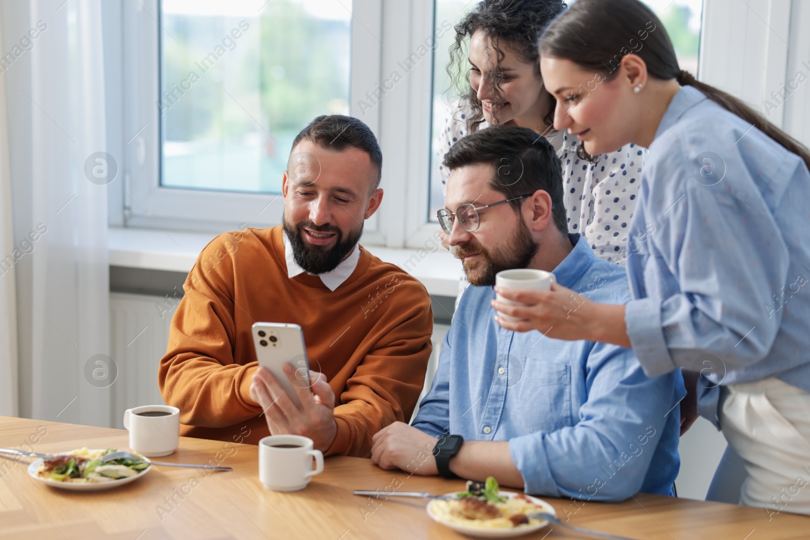 Photo of Man showing his colleagues something on smartphone during lunch break in office