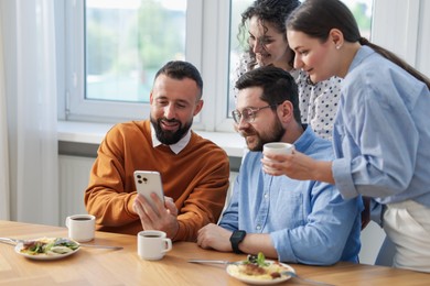 Photo of Man showing his colleagues something on smartphone during lunch break in office