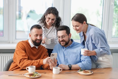 Photo of Man showing his colleagues something on smartphone during lunch break in office