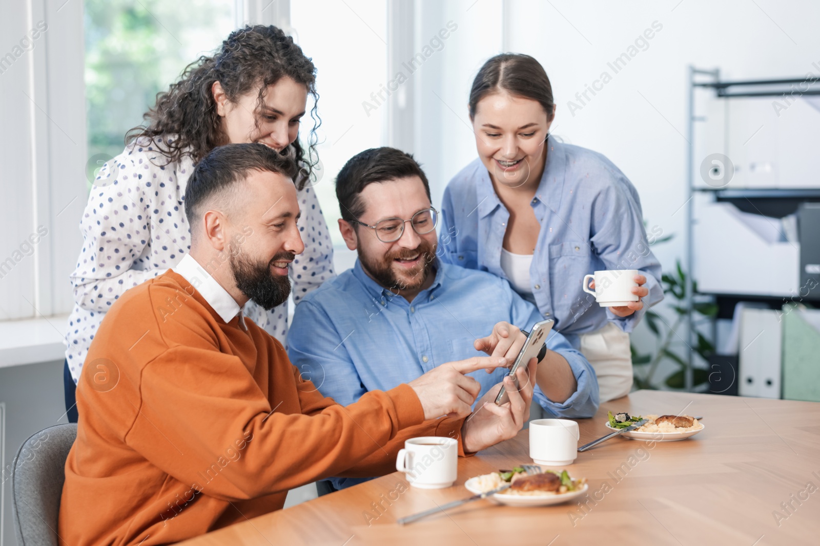 Man showing his colleagues something on smartphone during lunch break in office Photo of Man showing his colleagues something on smartphone during lunch break in office