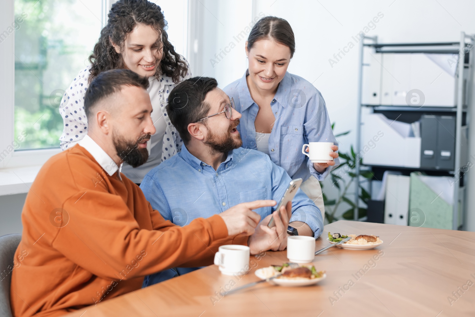 Man showing his colleagues something on smartphone during lunch break in office Photo of Man showing his colleagues something on smartphone during lunch break in office