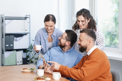 Photo of Man showing his colleagues something on smartphone during lunch break in office