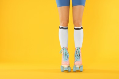 Photo of Woman in roller skates on orange background, closeup. Space for text