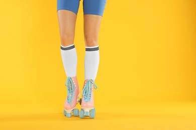 Photo of Woman in roller skates on orange background, closeup. Space for text