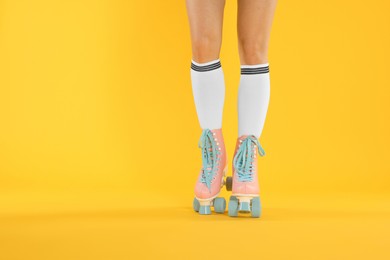 Photo of Woman in roller skates on orange background, closeup. Space for text