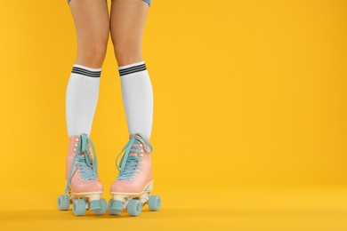 Photo of Woman in roller skates on orange background, closeup. Space for text