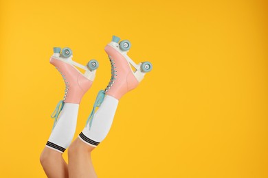 Photo of Woman in roller skates on orange background, closeup. Space for text
