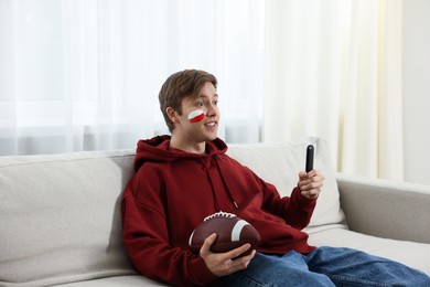 Photo of Emotional sports fan with remote control and ball watching game indoors