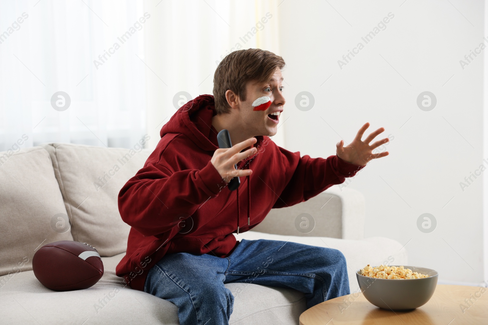 Emotional sports fan with remote control and ball watching game indoors Photo of Emotional sports fan with remote control and ball watching game indoors