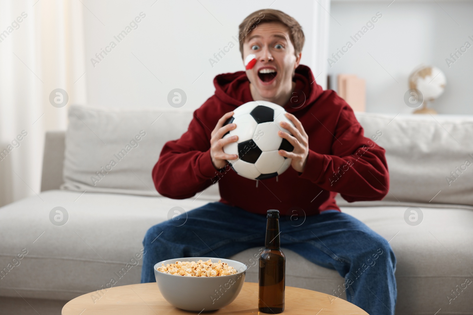 Photo of Emotional sports fan with soccer ball watching game indoors, selective focus