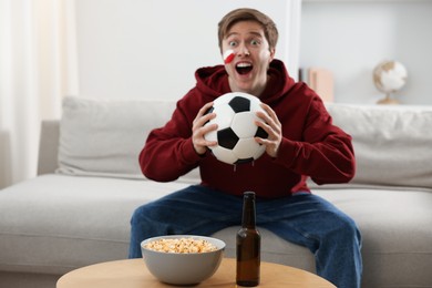 Photo of Emotional sports fan with soccer ball watching game indoors, selective focus