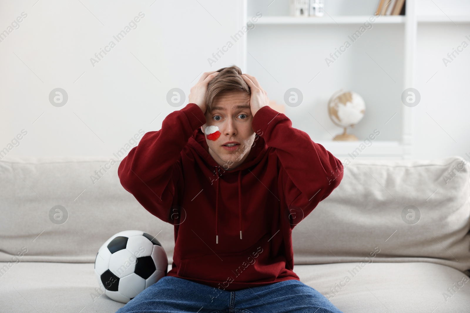 Photo of Emotional sports fan with soccer ball watching game indoors