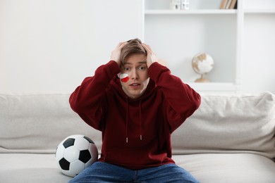 Photo of Emotional sports fan with soccer ball watching game indoors