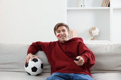 Photo of Sports fan with remote control and soccer ball watching game indoors