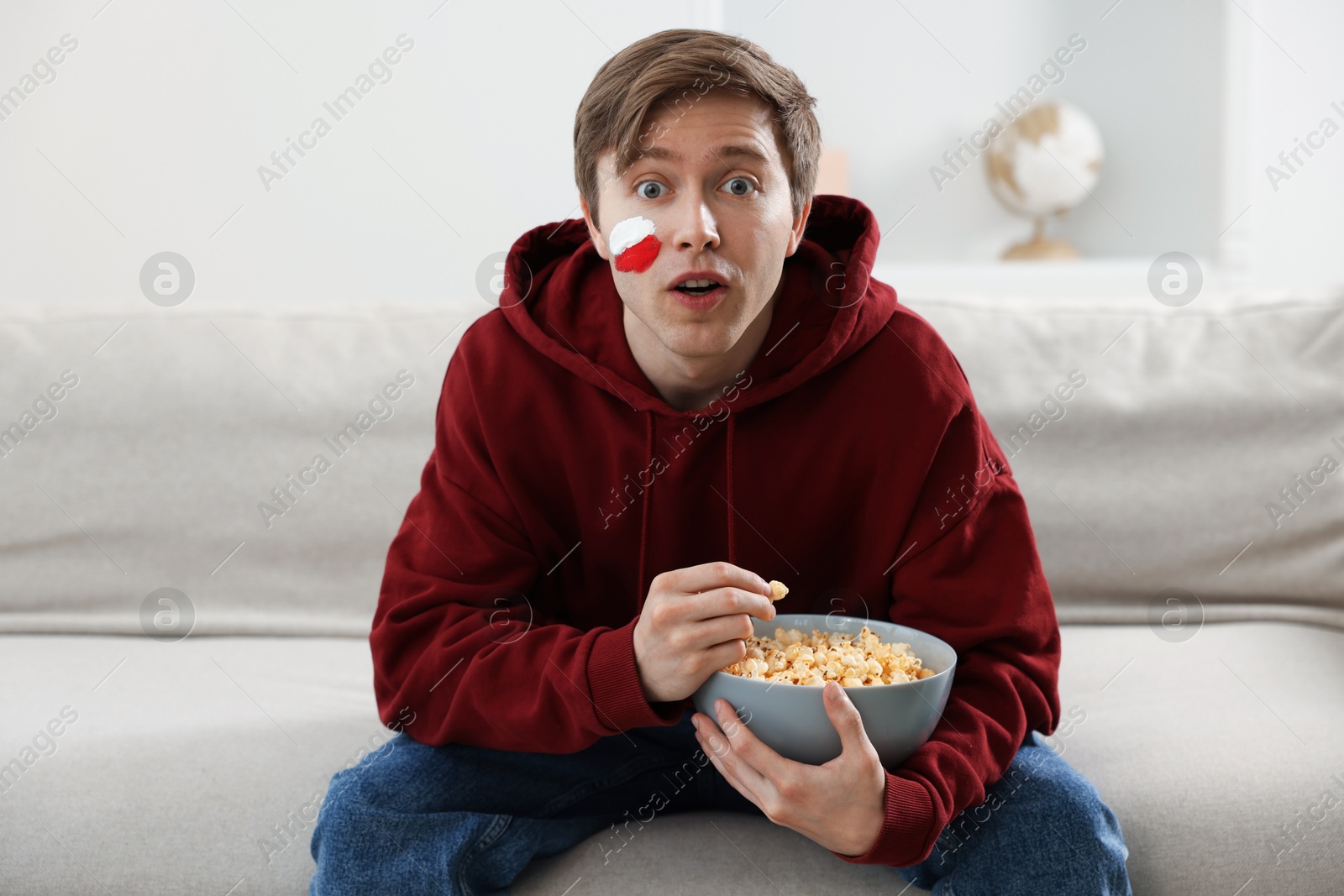 Photo of Sports fan eating popcorn while watching game on sofa indoors