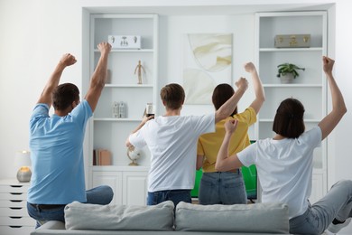 Photo of Group of football fans watching game together indoors, back view