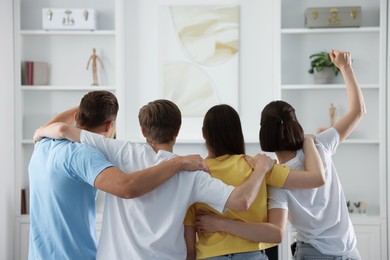 Photo of Group of football fans watching game together indoors, back view