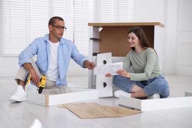 Photo of Happy couple assembling furniture on floor at home