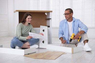 Photo of Happy couple assembling furniture on floor at home
