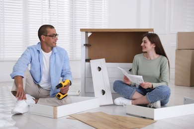 Photo of Happy couple assembling furniture on floor at home