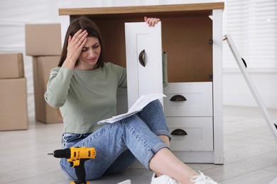 Photo of Upset woman with manual assembling furniture on floor at home