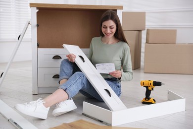Photo of Smiling woman with manual assembling furniture on floor at home