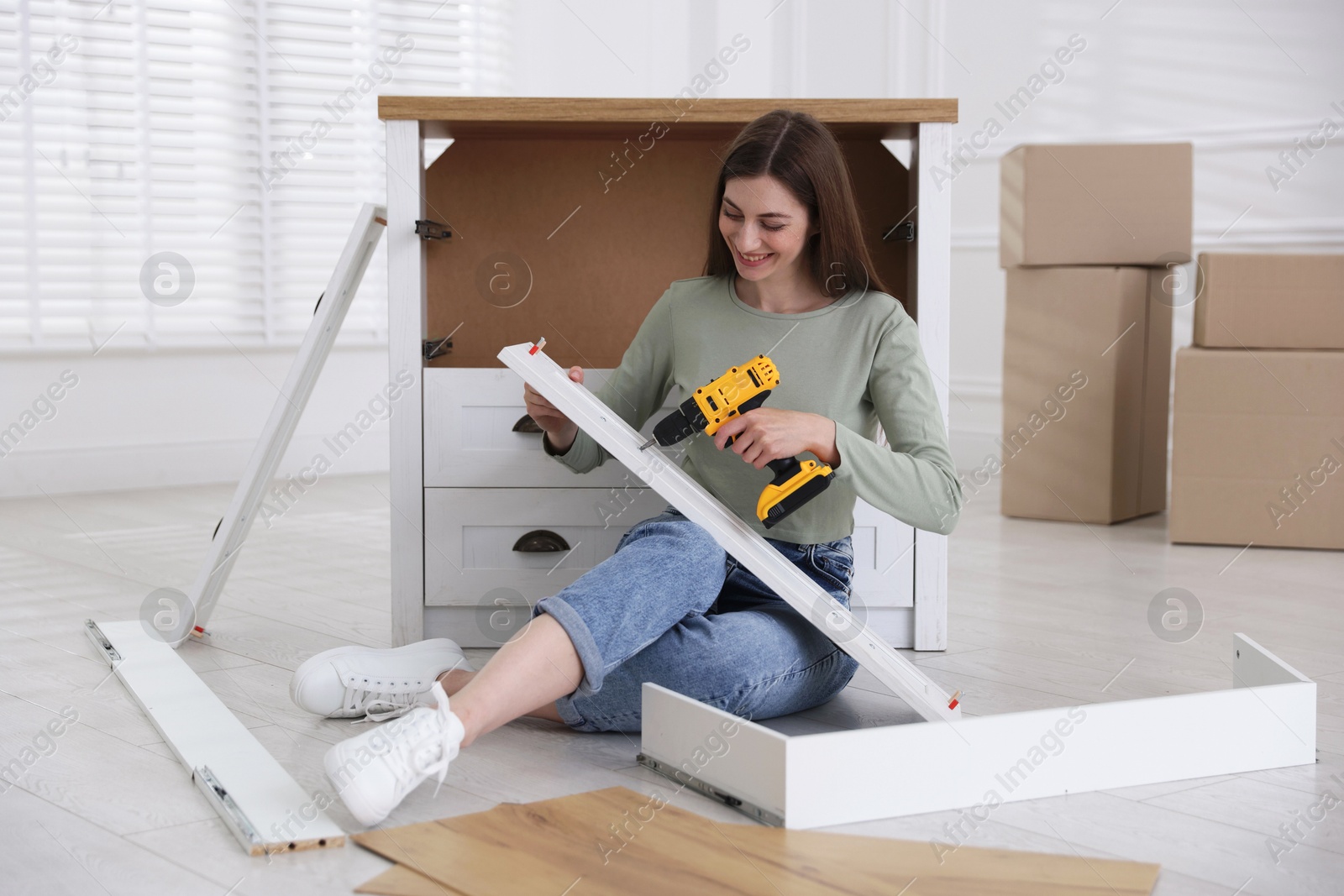 Smiling woman assembling furniture with electric screwdriver on floor at home Photo of Smiling woman assembling furniture with electric screwdriver on floor at home