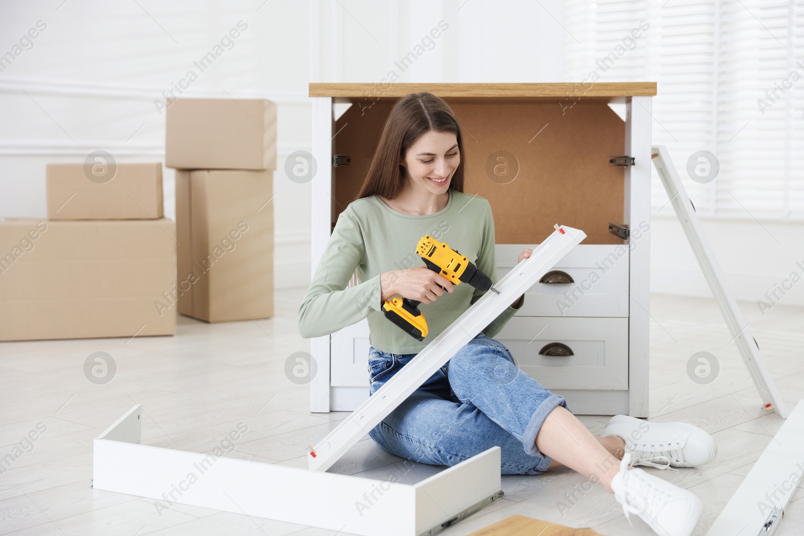 Smiling woman assembling furniture with electric screwdriver on floor at home Photo of Smiling woman assembling furniture with electric screwdriver on floor at home