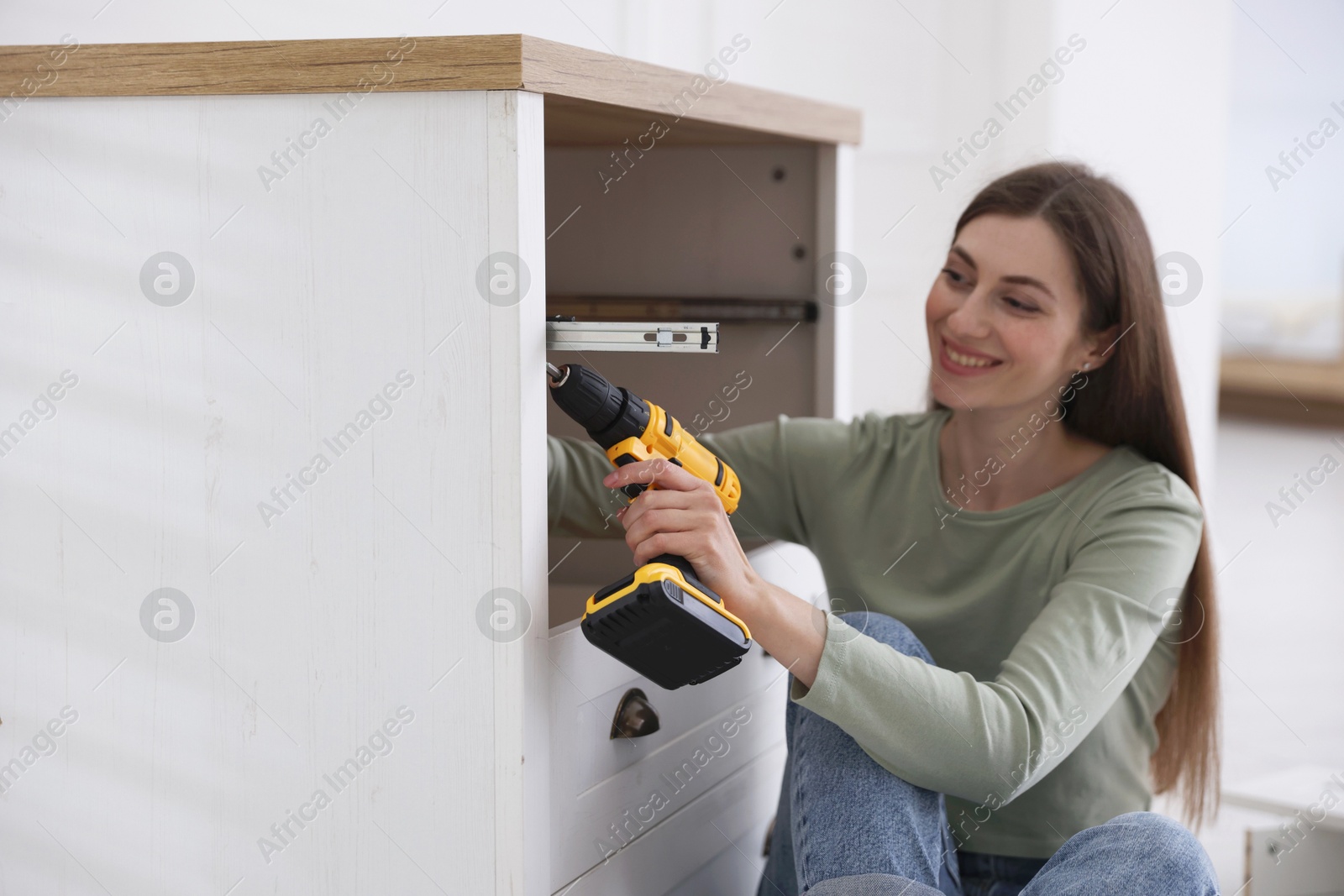 Smiling woman assembling furniture with electric screwdriver at home Photo of Smiling woman assembling furniture with electric screwdriver at home