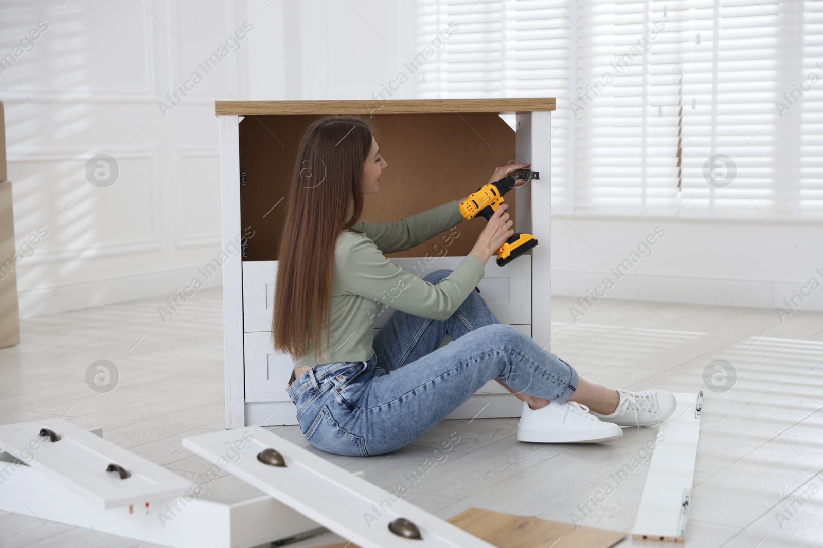 Woman assembling furniture with electric screwdriver on floor at home Photo of Woman assembling furniture with electric screwdriver on floor at home