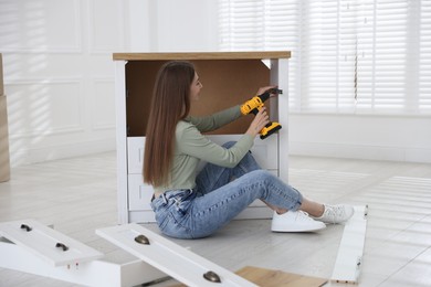 Photo of Woman assembling furniture with electric screwdriver on floor at home