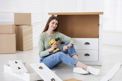 Photo of Woman assembling furniture with electric screwdriver on floor at home