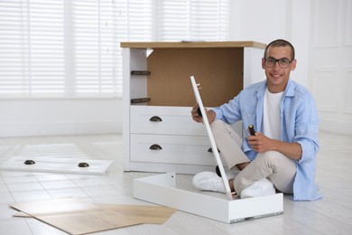 Photo of Smiling man assembling furniture with screwdriver on floor at home
