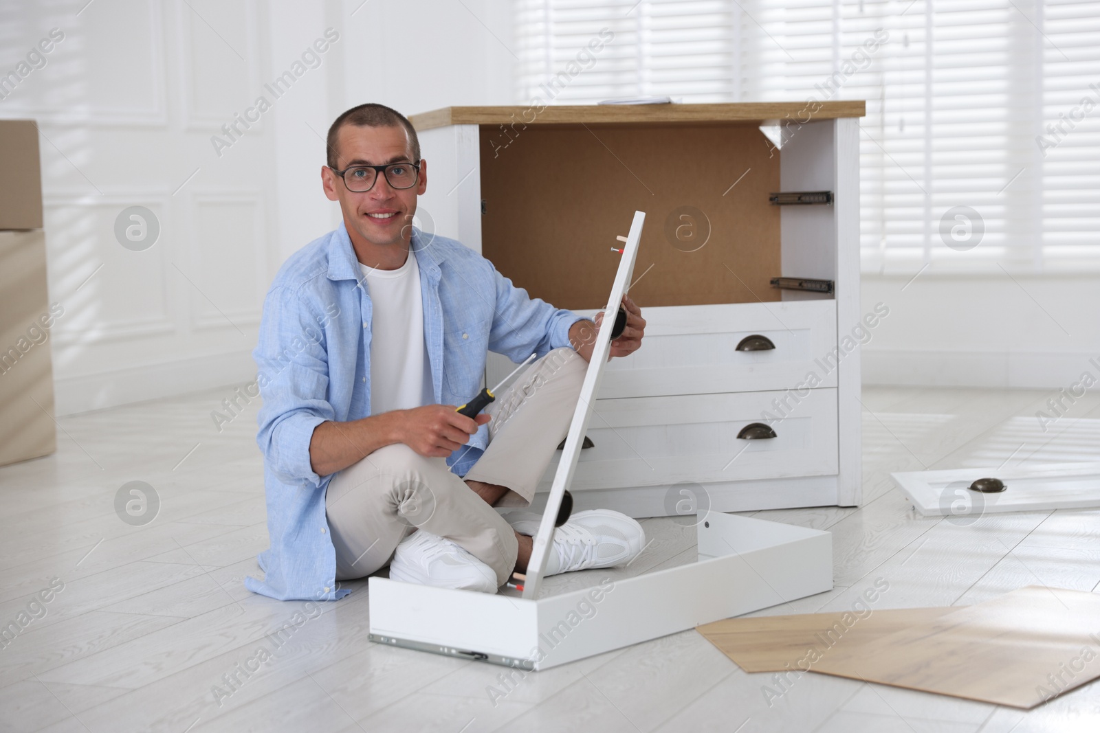 Smiling man assembling furniture with screwdriver on floor at home Photo of Smiling man assembling furniture with screwdriver on floor at home