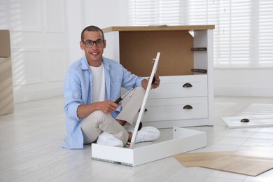 Photo of Smiling man assembling furniture with screwdriver on floor at home