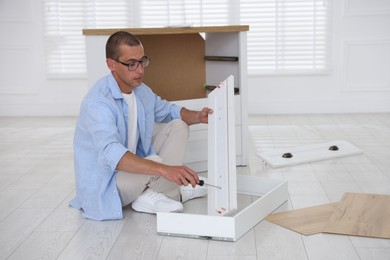 Photo of Man assembling furniture with screwdriver on floor at home