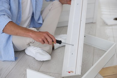 Photo of Man assembling furniture with screwdriver on floor at home, closeup