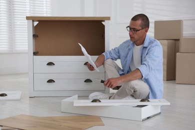 Photo of Man with manual and screwdriver assembling furniture on floor at home