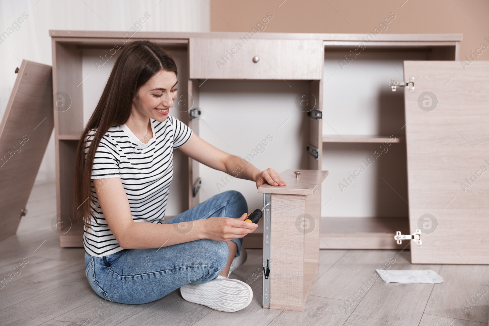 Smiling woman assembling furniture with screwdriver on floor at home Photo of Smiling woman assembling furniture with screwdriver on floor at home