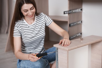 Photo of Smiling woman assembling furniture with screwdriver on floor at home
