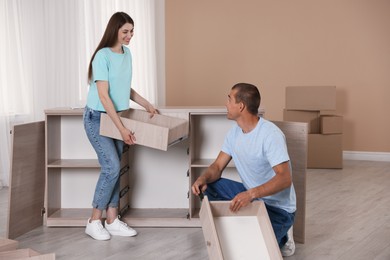 Photo of Happy couple assembling furniture on floor at home