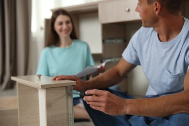 Photo of Couple assembling furniture with screwdriver on floor at home, selective focus
