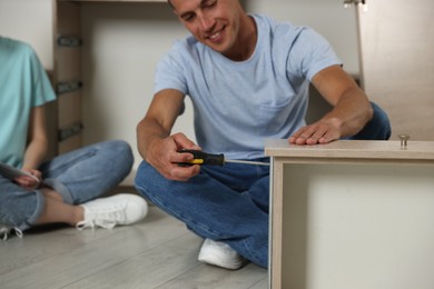 Photo of Smiling man assembling furniture with screwdriver and his wife on floor at home, selective focus