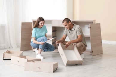 Photo of Happy couple with manual assembling furniture on floor at home