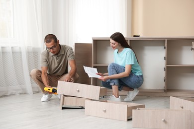 Photo of Happy couple with manual assembling furniture on floor at home
