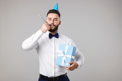 Photo of Happy Birthday. Handsome man with party hat, blower and gift box on grey background