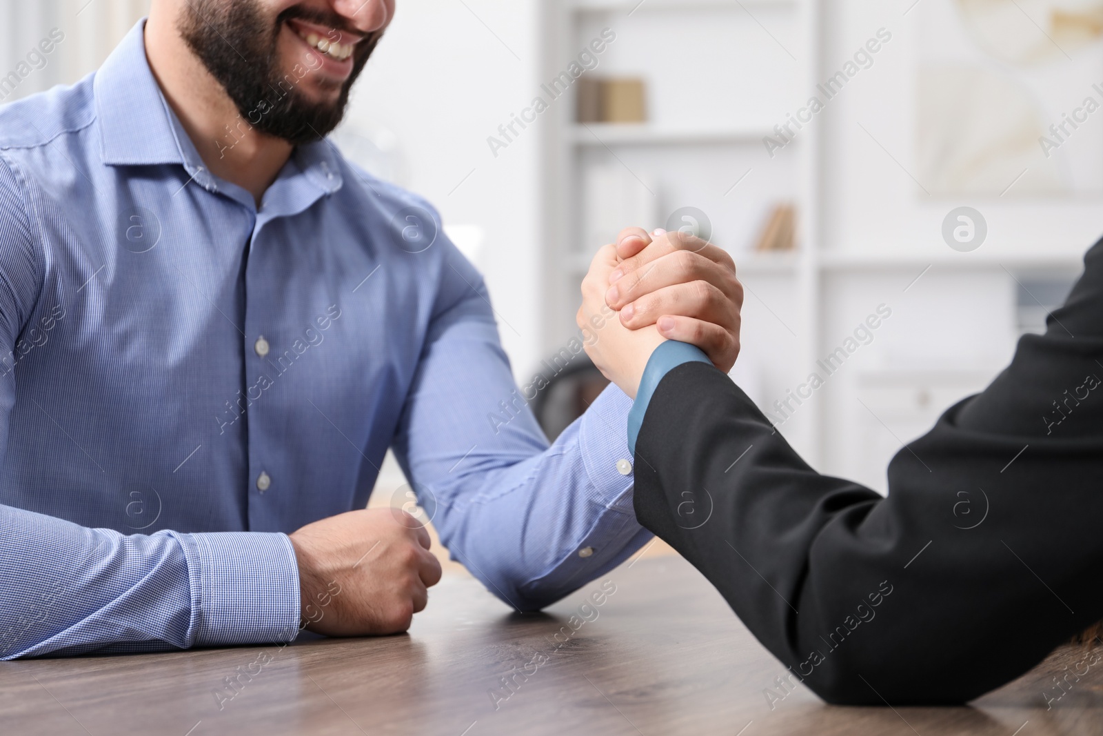 Businesspeople arm wrestling at wooden table in office, closeup Photo of Businesspeople arm wrestling at wooden table in office, closeup