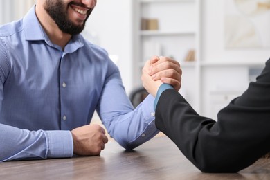 Photo of Businesspeople arm wrestling at wooden table in office, closeup