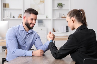 Photo of Businesspeople arm wrestling at wooden table in office