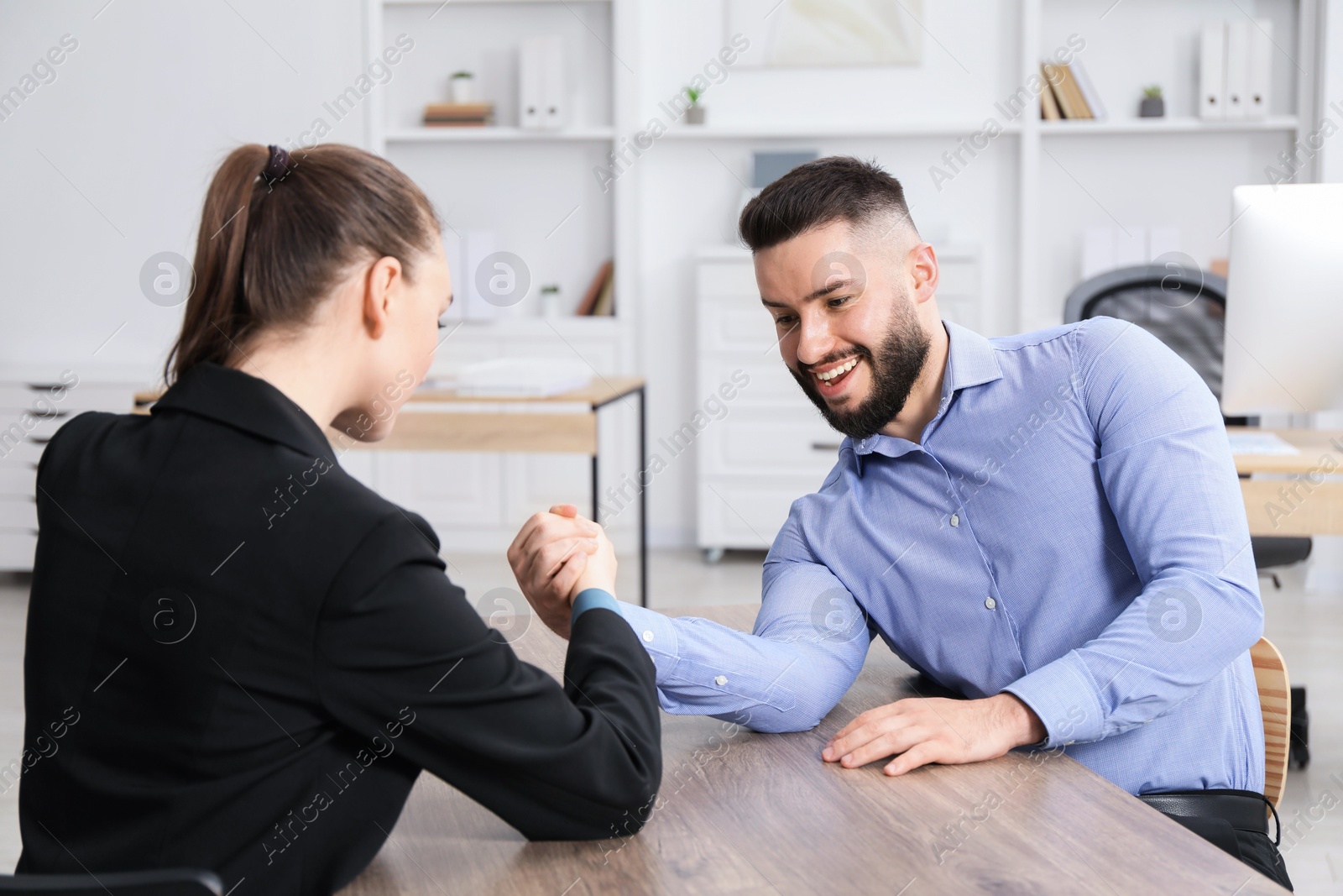 Businesspeople arm wrestling at wooden table in office Photo of Businesspeople arm wrestling at wooden table in office